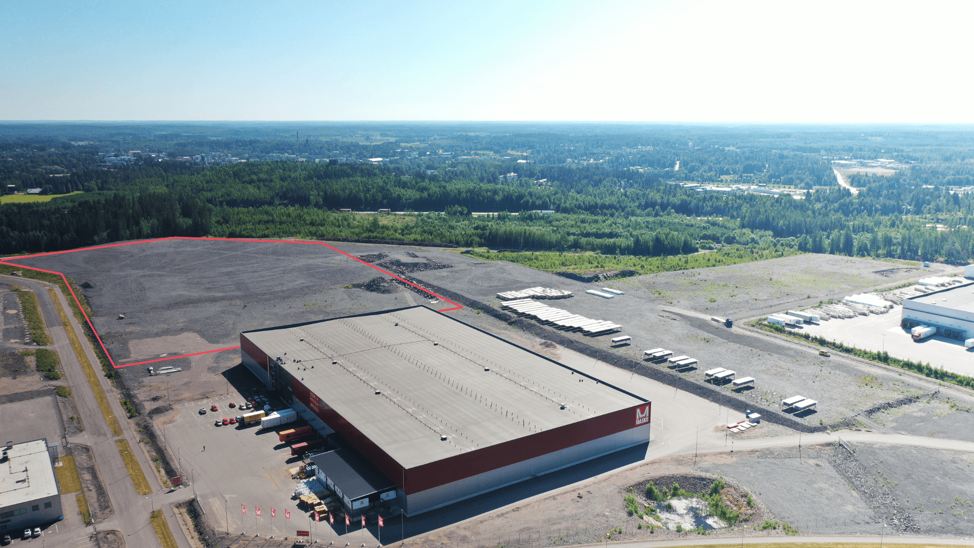 Havainnekuva datakeskushankkeelle suunnitellusta tontista Kapulin Yritysalueella. Ilmakuvassa näkyy Maskun logistiikkakeskus, jonka takana on datakeskukselle suunniteltu tasattu tontti.